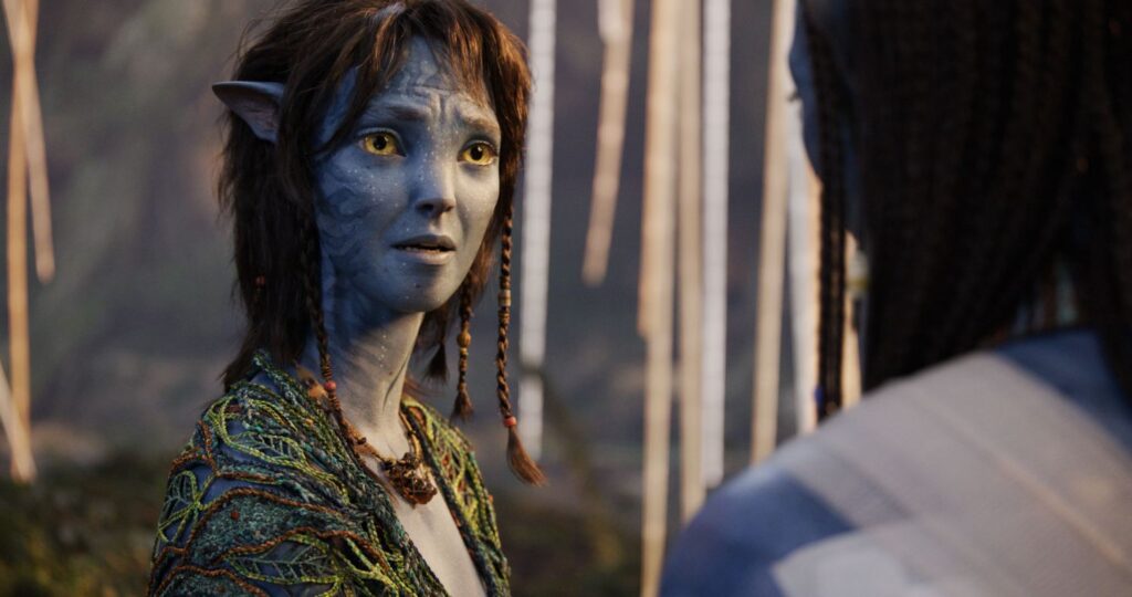 Kiri, a young Na'vi character with a worried expression and short brown hair, looks intently at another character off-screen inside a dense, glowing jungle environment.