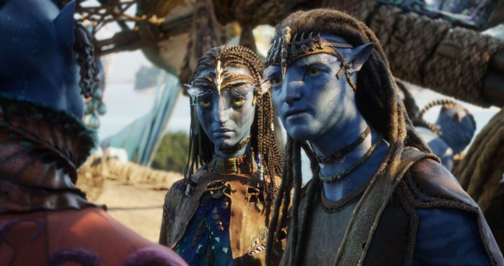 ake Sully and Neytiri in traditional Na'vi attire standing in an outdoor setting on Pandora while speaking with another Na'vi character, seen from behind.