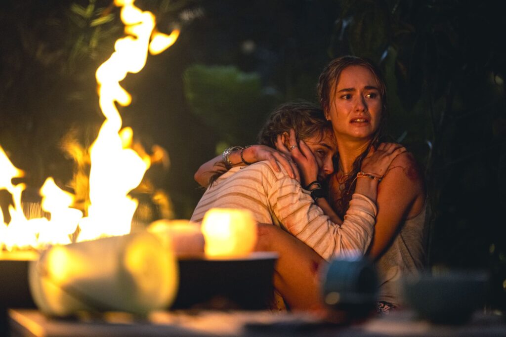Two young women embrace in fear beside a fire pit at night