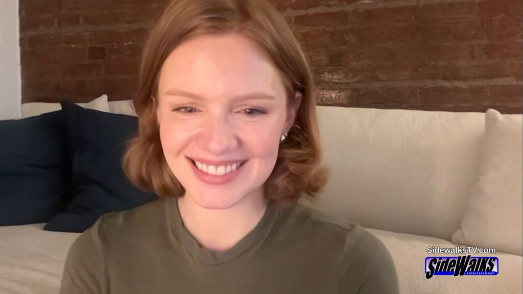 A smiling Scarlet Hunter in a green shirt, sitting on a couch in front of a brick wall.