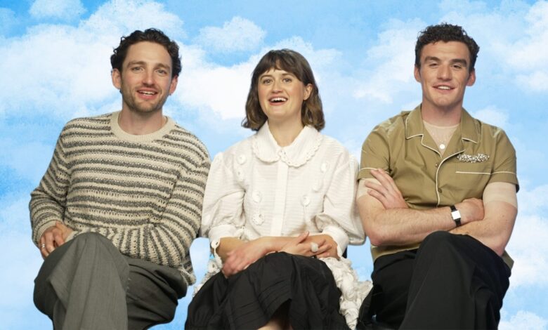 Laurie Davidson, Ella Bruccoleri, and Dónal Finn from The Other Bennet Sister sitting in chairs during the interview with a sky background.