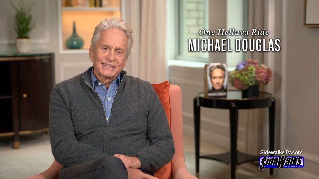 Michael Douglas smiling while sitting. His book and graphic are on the right side.