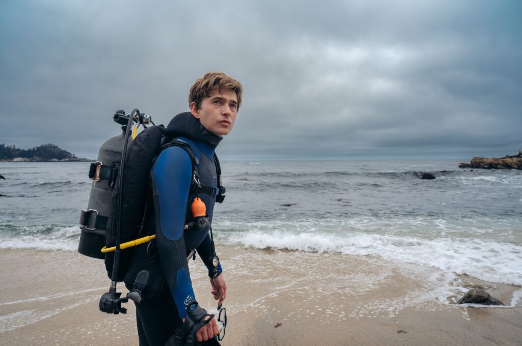 Austin Abrams as Jay Gardiner standing on the beach.